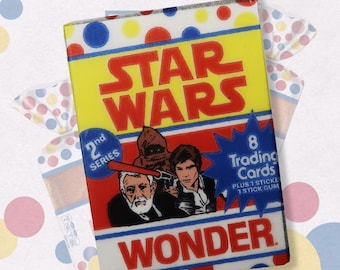 Puede incluir: Un paquete de cartas coleccionables de Star Wars vintage con un diseño amarillo, rojo y azul. El paquete presenta una imagen de Han Solo, Chewbacca y Obi-Wan Kenobi. El texto en el paquete dice "2nd Series", "8 Trading Cards", "Plus 1 Sticke 1 Stick Gum", y "Wonder".