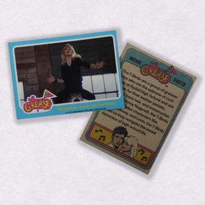 Puede incluir: Una tarjeta de intercambio vintage con una foto de una actriz de la pel&iacute;cula Grease. La tarjeta tiene un borde azul y el texto "Stephanie wants a Cool Rider!" La parte posterior de la tarjeta tiene un fondo marr&oacute;n con el texto "Grease" y "Movie Facts".