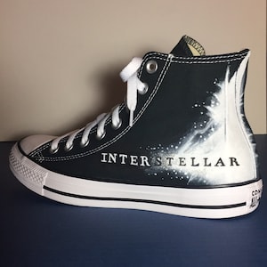 May include: Black high-top canvas sneakers with white paint splatters and the word "INTERSTELLAR" written in black.