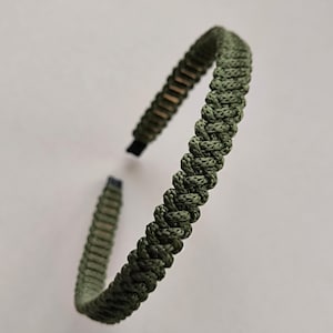 Op de afbeelding: Olijfgroene paracord armband. De armband is gemaakt van geweven koord en heeft een eenvoudig, minimalistisch ontwerp. De armband wordt getoond tegen een witte achtergrond.