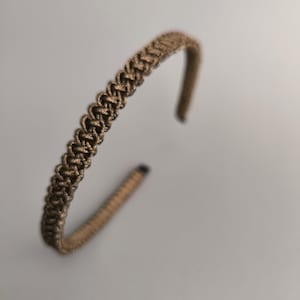 Può includere: Un cerchietto intrecciato marrone per capelli.