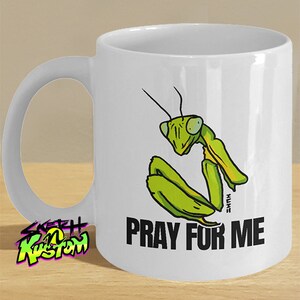 May include: White ceramic mug with a green praying mantis illustration and the text "Pray for me".