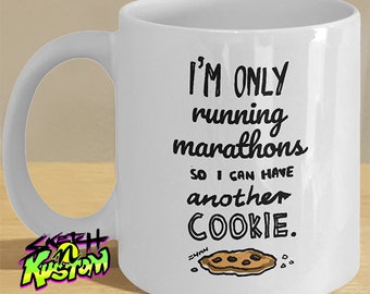 May include: White ceramic coffee mug with a black graphic that says "I'm only running marathons so I can have another cookie."  A cartoon cookie with chocolate chips is drawn below the text. The mug has a black and green logo on the side that says "Sketch n Kustom".
