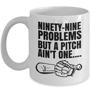 May include: White ceramic coffee mug with a black graphic of a baseball bat and glove. The text on the mug reads "Ninety-nine problems but a pitch ain't one..."