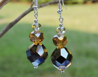 May include: A pair of silver dangle earrings with three crystal beads each. The top bead is clear, the middle bead is amber, and the bottom bead is a dark, faceted crystal.