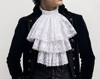 May include: A black velvet coat with ornate metal buttons and embroidered cuffs, worn over a dark patterned vest and a white shirt featuring a multi-layered, ruffled lace jabot at the neck and matching lace trim at the sleeve cuffs.