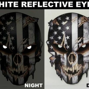 May include: A black and white skull with a distressed American flag design. The skull has white reflective eyes that glow in the dark. The skull is shown in both day and night views.