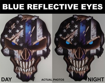 May include: A skull with a cracked American flag design and a blue line down the center. The skull has reflective blue eyes that glow in the dark. The image shows the skull in both daylight and nighttime.