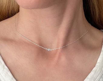 May include: A silver chain necklace with a single small, clear gemstone pendant.