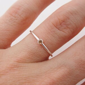 May include: A simple silver band ring with a small, round, brown gemstone.