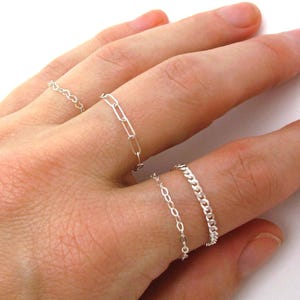 May include: A hand wearing four silver chain rings. The rings are stacked on the middle finger.