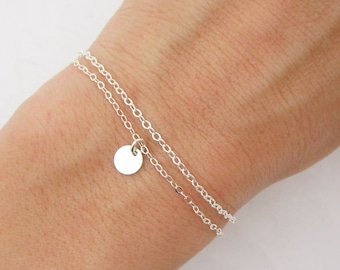 May include: A silver chain bracelet with a small, round charm. The bracelet is layered with two chains.