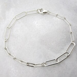 May include: A silver chain bracelet with a simple, linked design. The bracelet is made of oval-shaped links.