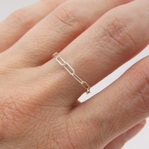 May include: A silver chain ring worn on a finger.