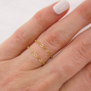 May include: A gold chain ring with two delicate chains layered on top of each other. The ring is worn on a finger.