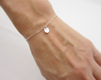 May include: A delicate silver chain bracelet with a small, round charm hanging from it.