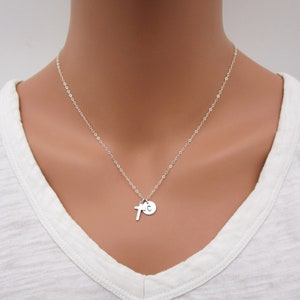 May include: A silver chain necklace with a small silver cross charm and a silver disc charm with the letter "C" engraved on it.