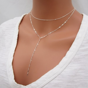 May include: A silver layered necklace with a long pendant chain. The necklace is made of delicate, linked chains.