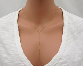 May include: A gold chain necklace with a long, thin pendant. The necklace is on a white background.