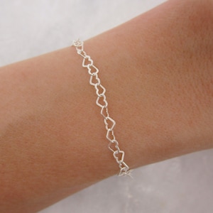 May include: A silver heart-shaped chain bracelet. The bracelet is made of small, delicate hearts that are linked together.
