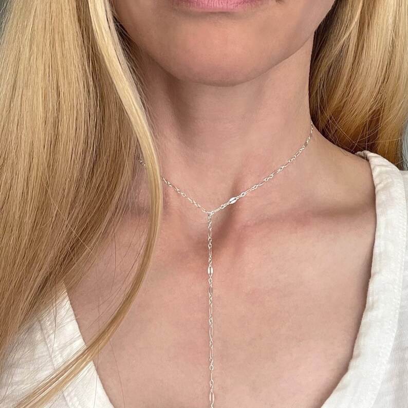 May include: A silver chain necklace with a delicate, Y-shaped design. The necklace is made of small, oval-shaped links and has a long, dangling pendant.