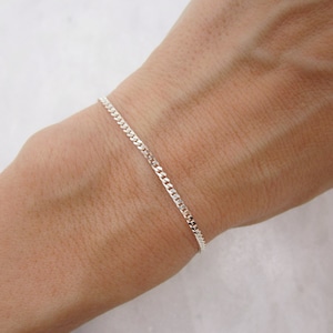 K&ouml;nnte beinhalten: Ein zartes Armband mit Silber-Kettenmuster. Das Armband ist d&uuml;nn und liegt am Handgelenk an. Die Glieder sind klein und eng miteinander verbunden, wodurch eine glatte, durchgehende Linie entsteht. Das Armband ist ein schlichtes, elegantes Schmuckst&uuml;ck.