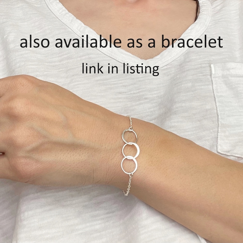 Pode incluir: Um bracelete de corrente de prata com tr&ecirc;s c&iacute;rculos entrela&ccedil;ados. O bracelete &eacute; mostrado no pulso de uma pessoa.  also available as a bracelet link in listing