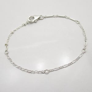 May include: A silver chain bracelet featuring a mix of link styles, including small heart-shaped links, elongated oval links, and round beads. The bracelet is secured with a silver lobster claw clasp that is stamped with the number 925.