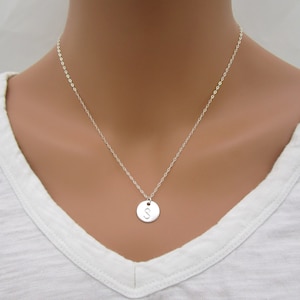 May include: A silver chain necklace with a silver pendant featuring the letter "S" engraved on a round disc.