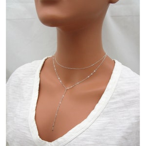 May include: A silver layered necklace with a long pendant chain. The necklace is made of delicate chains with small oval links.