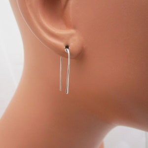 May include: A pair of simple silver earrings with a curved wire design. The earrings are shown on a mannequin's ear.