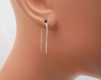 May include: A pair of simple silver earrings with a curved wire design. The earrings are shown on a mannequin's ear.