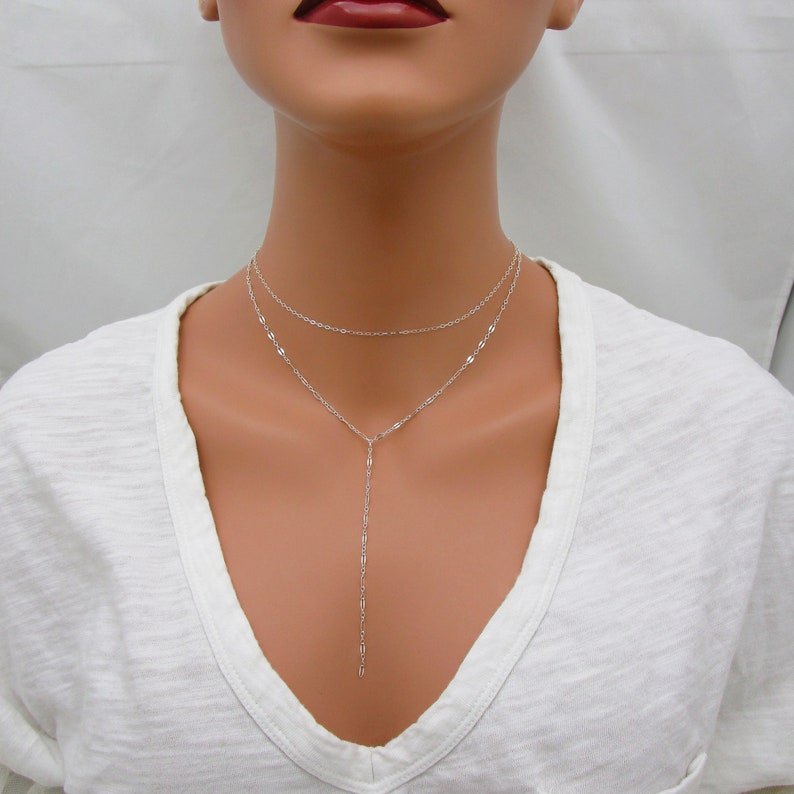 May include: A silver layered necklace with a long pendant chain. The necklace is made of delicate chains and has a simple, minimalist design.