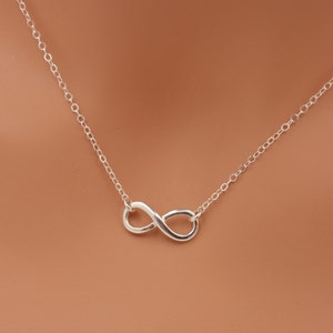 May include: A silver infinity symbol necklace on a brown background.