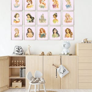 May include: A collection of framed watercolor portraits of various princesses, displayed on a white wall. The portraits feature the princesses with different hairstyles and gowns. The room also includes a wooden cabinet, a white chair, and decorative items.