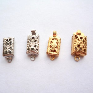 May include: Four metal clasps with intricate designs. Two are silver and two are gold. Each clasp has a rectangular shape with a decorative openwork pattern.