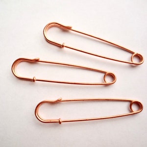 May include: Three rose gold safety pins, each with a different size.