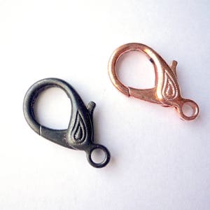 May include: Two metal lobster clasps, one black and one rose gold. Both clasps have a decorative design.