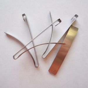 Op de afbeelding: Drie zilveren metalen clips, twee zijn gebogen en &eacute;&eacute;n is recht.