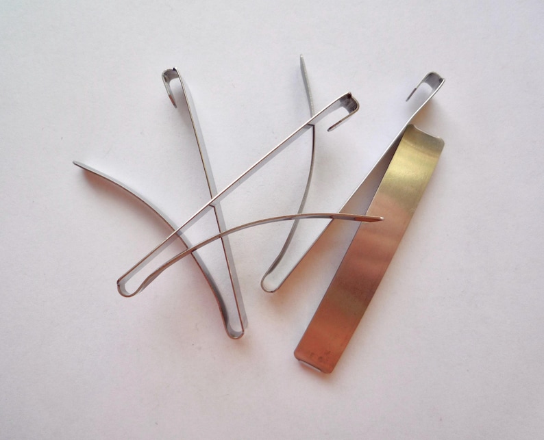 Op de afbeelding: Drie zilveren metalen clips, twee zijn gebogen en &eacute;&eacute;n is recht.