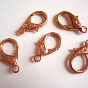 May include: Five copper-colored lobster clasps with a paisley design. The clasps are approximately 1 inch in length.
