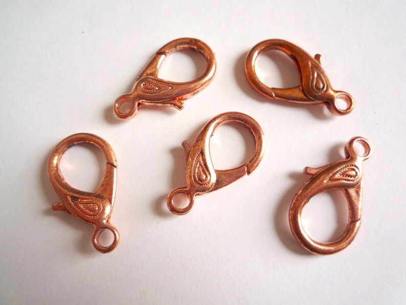 May include: Five copper-colored lobster clasps with a paisley design. The clasps are approximately 1 inch in length.