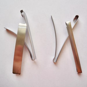 Op de afbeelding: Drie zilveren metalen haarclips. Twee van de clips zijn gebogen in een U-vorm en de derde clip is recht.