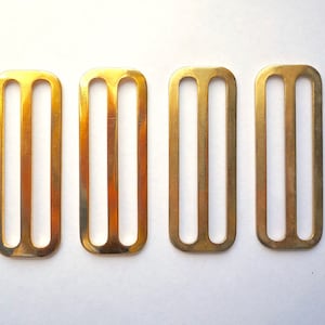 May include: Four gold-colored metal slider buckles. Each buckle has three horizontal slots.