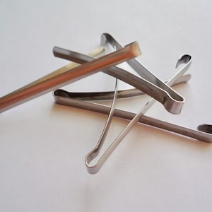 Op de afbeelding: Een set van vijf zilveren metalen haarclips. De clips zijn allemaal in verschillende maten en vormen en liggen op een witte ondergrond.