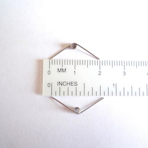May include: A silver spring with two coils, measured against a ruler marked in inches and millimeters. The spring is approximately 1 inch long.