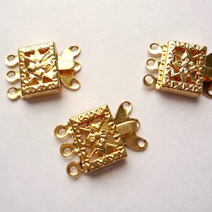 May include: Three gold-tone metal clasps with a decorative floral design. Each clasp has four loops for attaching jewelry.