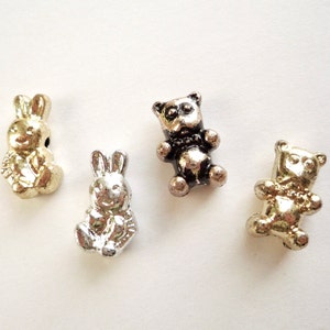 May include: Four metal charms in the shape of a bear and bunny. The charms are silver and gold in color.