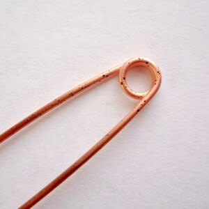 May include: A copper safety pin with a rounded head and a smooth, shiny finish.
