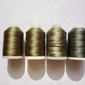 May include: Four spools of thread in shades of green. The spools are arranged in a row from left to right.